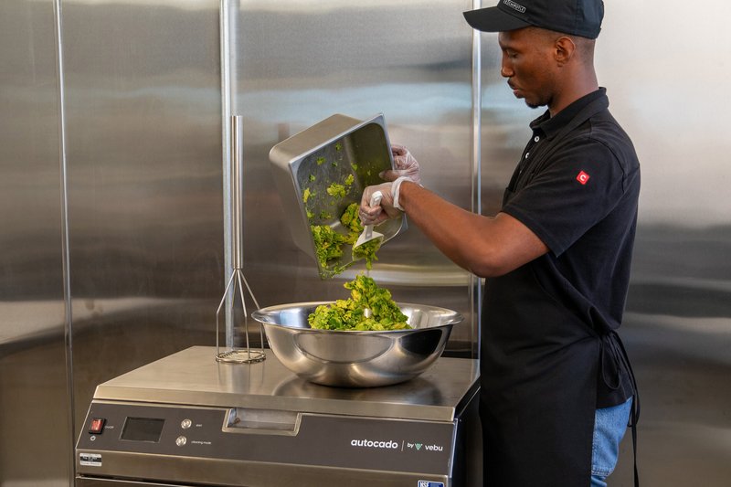 Autocado avocado-processing robot by Vebu: a Chipotle worker tipping avocado into the stainless steel machine